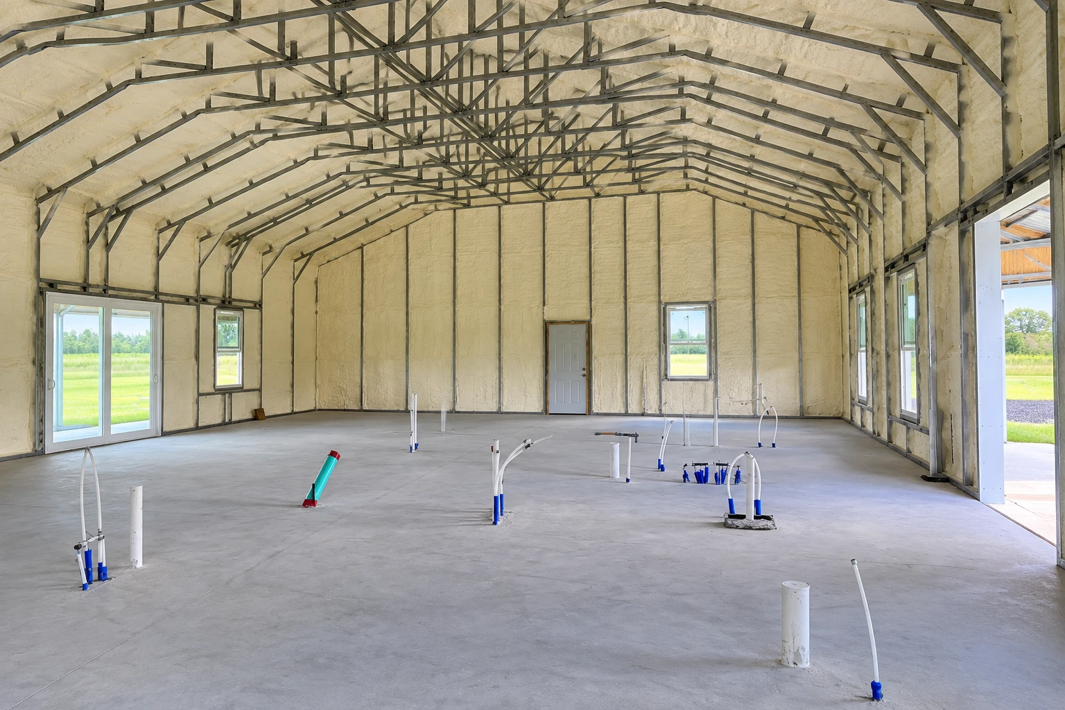A large unfinished commercial building has foam insulation covering its walls and arched ceiling above a concrete floor.