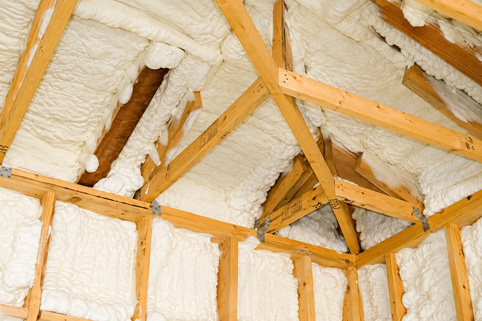 Open-cell spray foam fills the roof and wall cavities between exposed wooden rafters and studs.